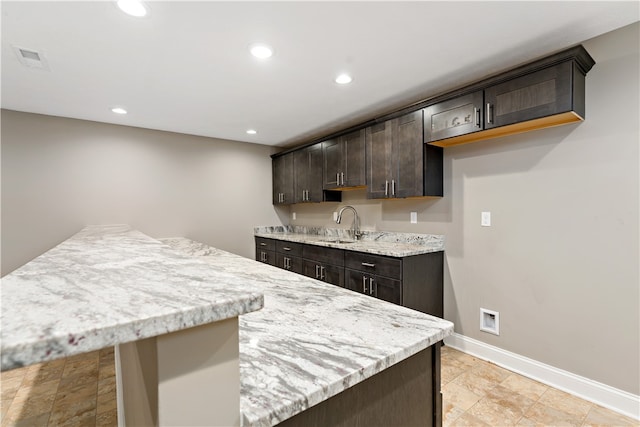 kitchen with dark brown cabinets, sink, and light stone counters