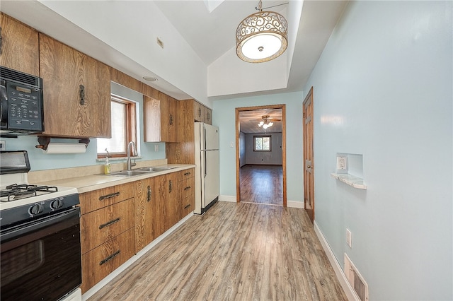 kitchen featuring sink, black appliances, decorative light fixtures, light hardwood / wood-style floors, and lofted ceiling