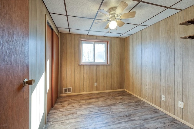 empty room featuring wood walls, light hardwood / wood-style flooring, and a drop ceiling