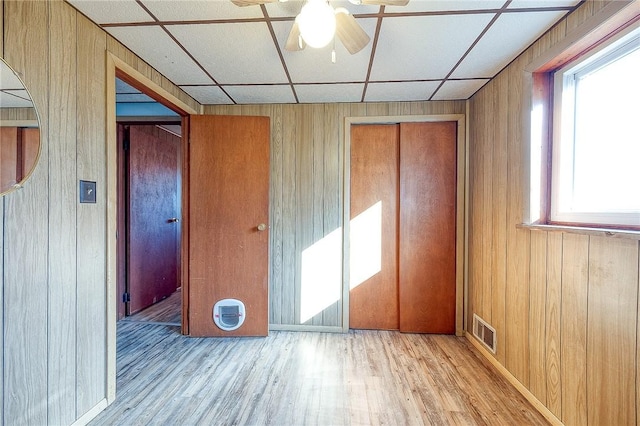 unfurnished bedroom with light hardwood / wood-style floors, a drop ceiling, and wooden walls