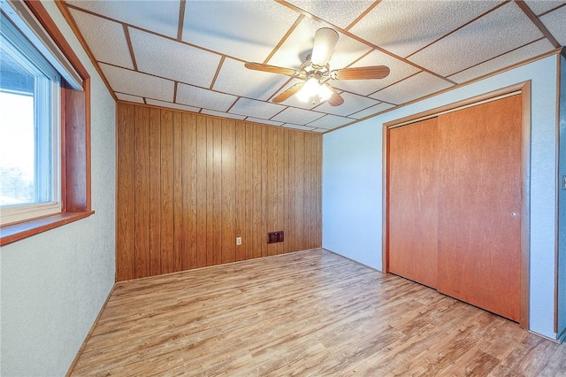 unfurnished bedroom featuring a closet, wood walls, light hardwood / wood-style flooring, and ceiling fan