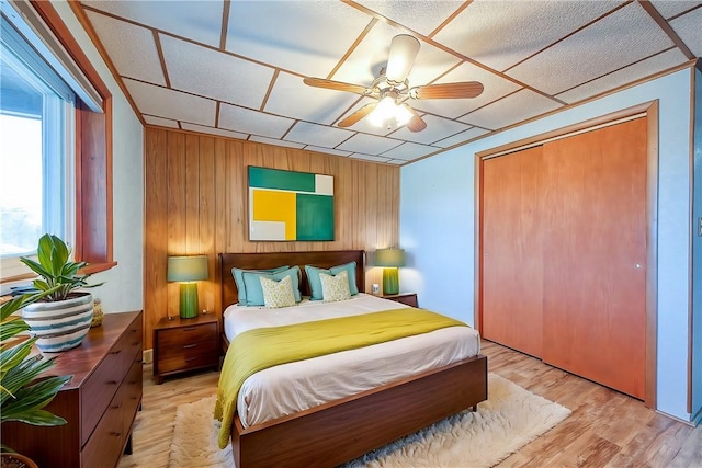 bedroom featuring light wood-type flooring, a closet, ceiling fan, and wood walls