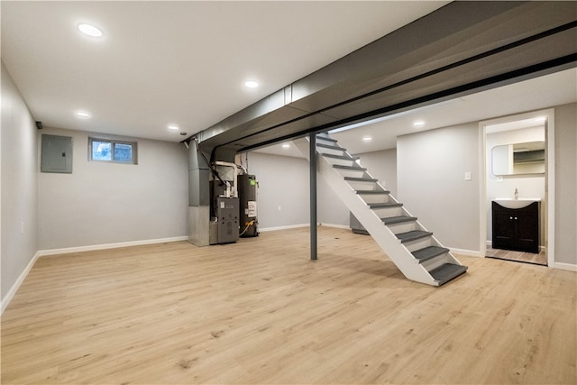 basement featuring electric panel, water heater, heating unit, and light hardwood / wood-style flooring