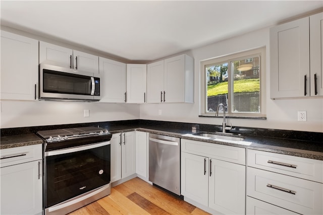 kitchen featuring stainless steel appliances, light hardwood / wood-style floors, white cabinets, sink, and dark stone countertops