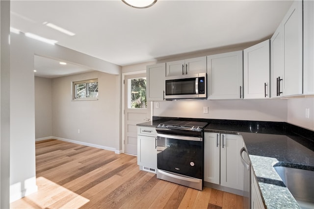 kitchen with white cabinetry, appliances with stainless steel finishes, light hardwood / wood-style floors, and dark stone countertops