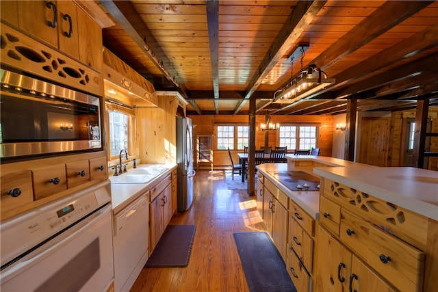 kitchen with light hardwood / wood-style floors, wood walls, sink, pendant lighting, and appliances with stainless steel finishes