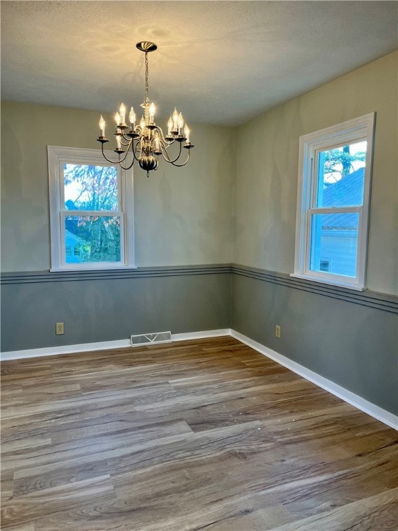 empty room with a wealth of natural light, hardwood / wood-style flooring, and a notable chandelier