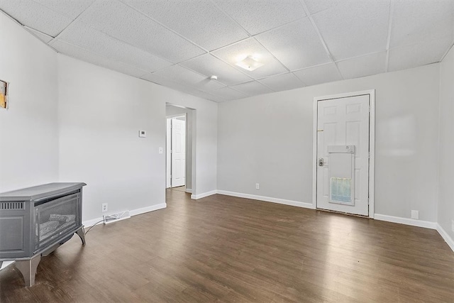 empty room featuring dark hardwood / wood-style flooring, a paneled ceiling, and a wood stove