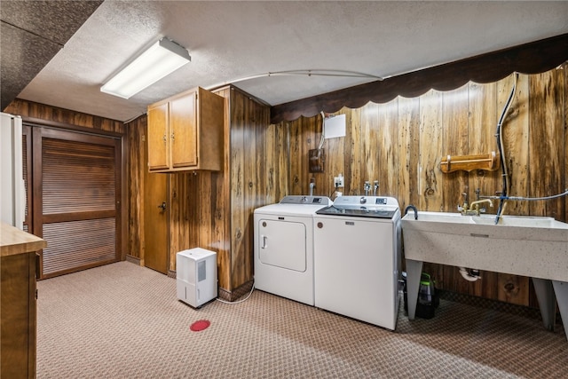 laundry area with wood walls, washing machine and dryer, light colored carpet, and a textured ceiling