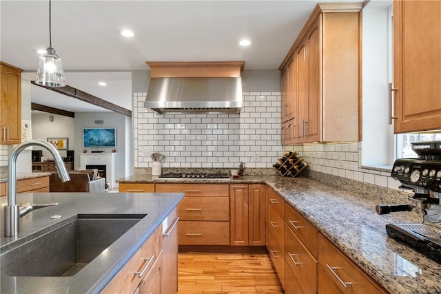 kitchen featuring light hardwood / wood-style floors, stainless steel gas cooktop, sink, wall chimney range hood, and dark stone countertops