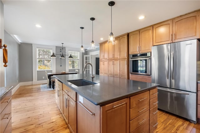 kitchen with a kitchen island with sink, appliances with stainless steel finishes, sink, and light hardwood / wood-style flooring