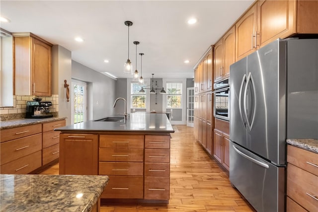 kitchen with stainless steel appliances, a center island with sink, decorative backsplash, sink, and light hardwood / wood-style flooring