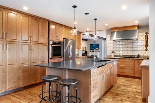 kitchen with stainless steel appliances, a kitchen island with sink, sink, and light wood-type flooring