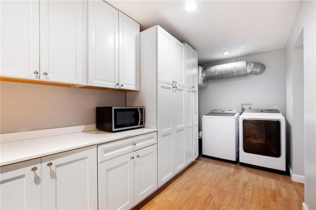 washroom with washing machine and dryer, cabinets, and light hardwood / wood-style floors