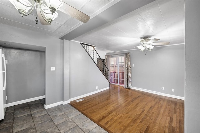 basement featuring wood-type flooring, white fridge, and ceiling fan with notable chandelier