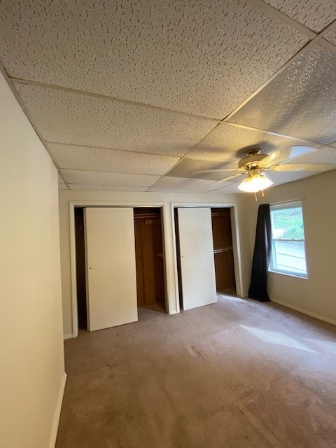 unfurnished bedroom with carpet flooring, a drop ceiling, two closets, and ceiling fan