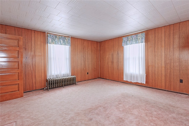 unfurnished room with a wealth of natural light, radiator heating unit, and wooden walls