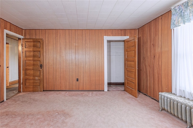 unfurnished bedroom featuring radiator heating unit, wooden walls, and multiple windows