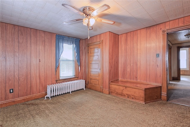 spare room with ceiling fan, carpet flooring, radiator heating unit, and wooden walls