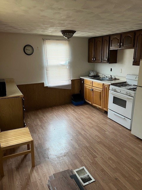 kitchen with white appliances, wooden walls, sink, and light wood-type flooring