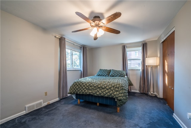 bedroom with multiple windows, dark colored carpet, and ceiling fan