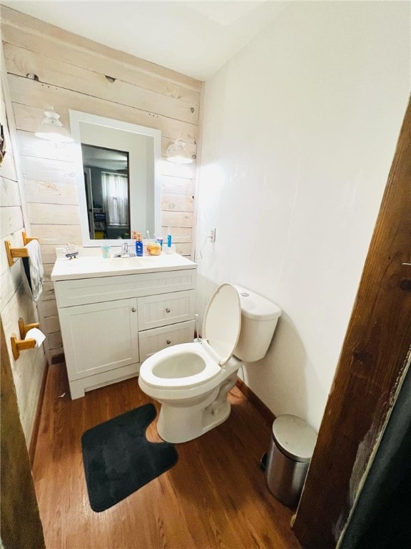 bathroom with hardwood / wood-style floors, wood walls, toilet, and vanity