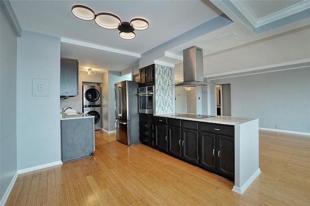 kitchen with sink, island exhaust hood, stacked washer and dryer, appliances with stainless steel finishes, and light wood-type flooring