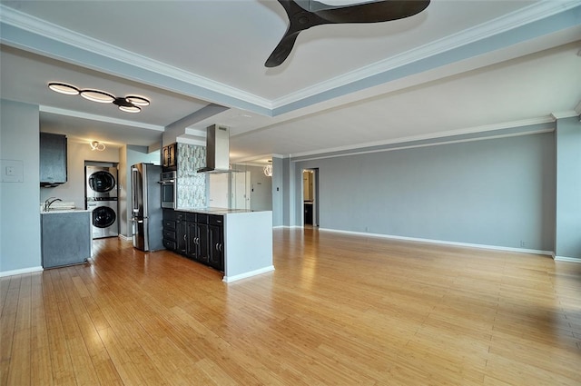 unfurnished living room featuring stacked washing maching and dryer, light hardwood / wood-style flooring, ceiling fan, and crown molding