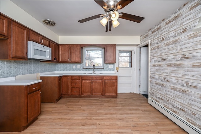 kitchen with sink, tasteful backsplash, ceiling fan, baseboard heating, and light wood-type flooring