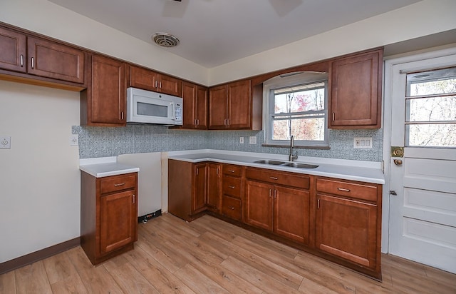 kitchen with light wood-type flooring, plenty of natural light, sink, and backsplash