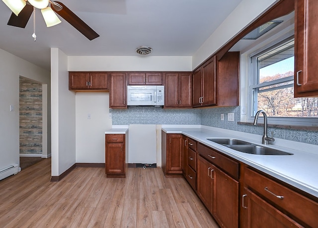 kitchen featuring sink, ceiling fan, backsplash, light hardwood / wood-style flooring, and a baseboard heating unit