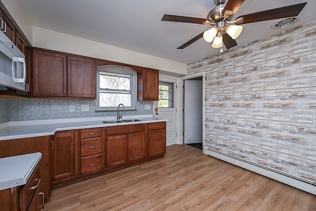 kitchen featuring backsplash, sink, baseboard heating, and light hardwood / wood-style flooring