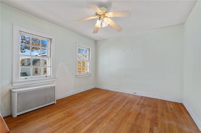 unfurnished room with light wood-type flooring, ceiling fan, and radiator