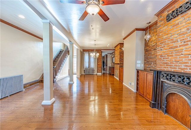 unfurnished living room featuring radiator, crown molding, ornate columns, light hardwood / wood-style floors, and brick wall