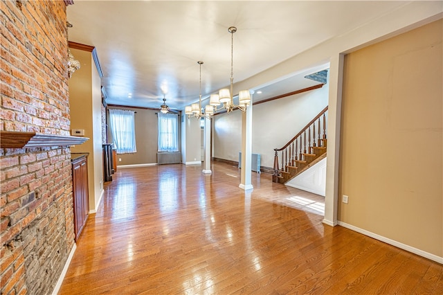 interior space with ornamental molding, hardwood / wood-style floors, ceiling fan with notable chandelier, and ornate columns