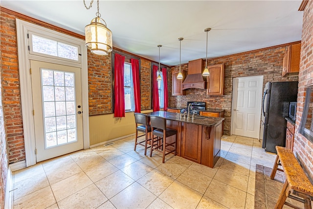 kitchen featuring pendant lighting, custom range hood, black appliances, and brick wall