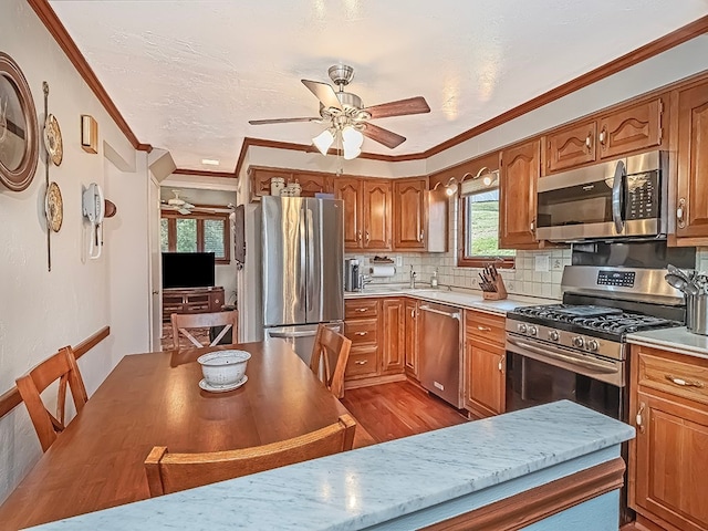 kitchen with crown molding, light wood-type flooring, appliances with stainless steel finishes, decorative backsplash, and ceiling fan