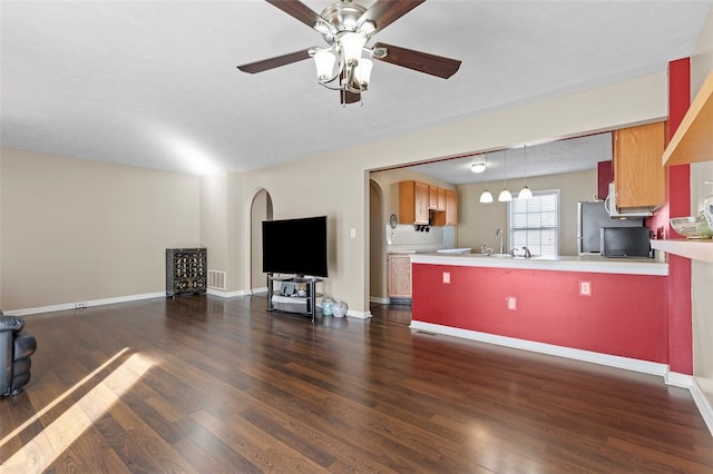 unfurnished living room featuring dark wood-type flooring, ceiling fan, and sink