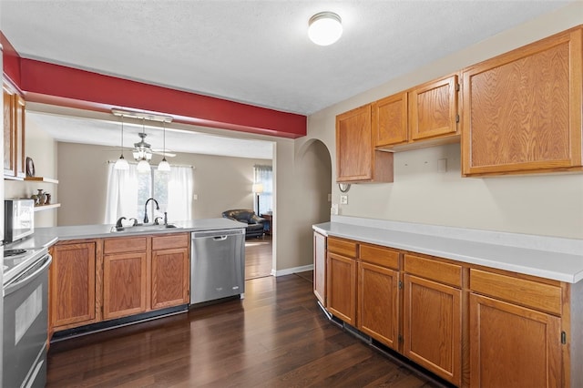 kitchen with dark wood-type flooring, kitchen peninsula, hanging light fixtures, sink, and appliances with stainless steel finishes