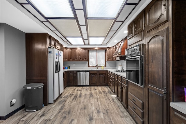 kitchen with dark brown cabinets, stainless steel appliances, light hardwood / wood-style floors, and sink