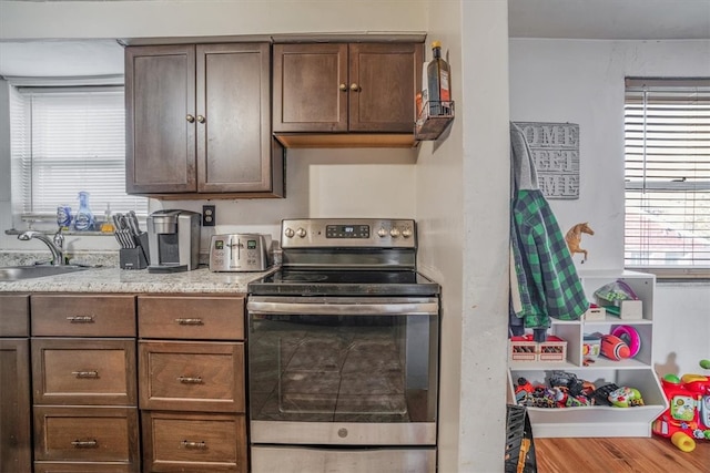 kitchen featuring light wood-type flooring, dark brown cabinets, light stone countertops, sink, and stainless steel electric stove