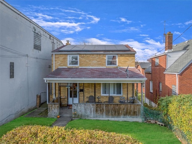 rear view of house with a lawn, solar panels, and covered porch