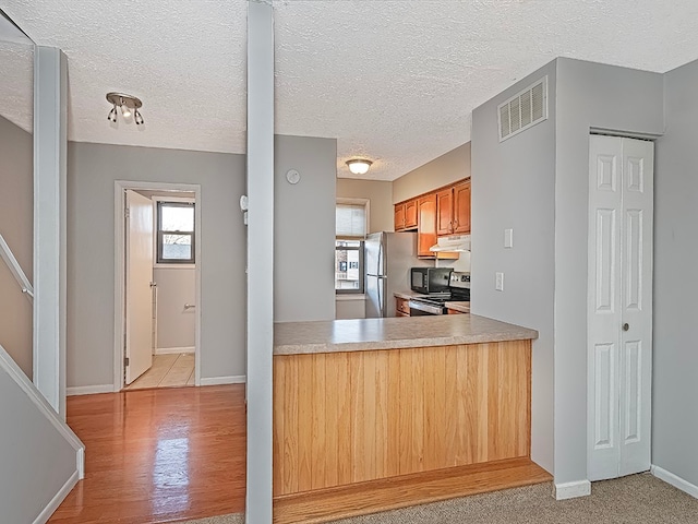 kitchen featuring light hardwood / wood-style floors, stainless steel refrigerator, a healthy amount of sunlight, and black range oven