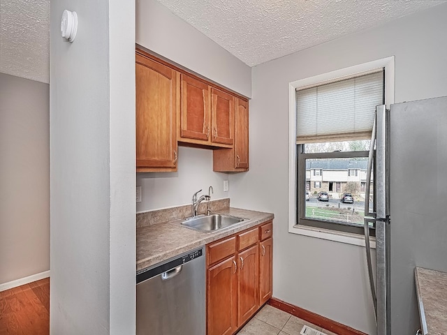 kitchen with stainless steel appliances, a textured ceiling, sink, and light wood-type flooring