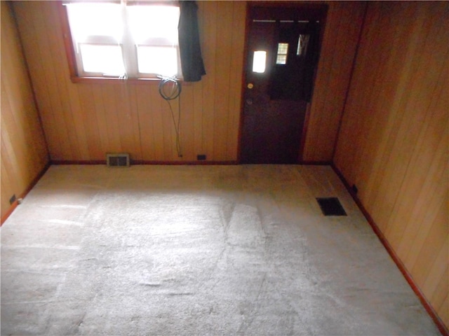 unfurnished room featuring light carpet and wooden walls