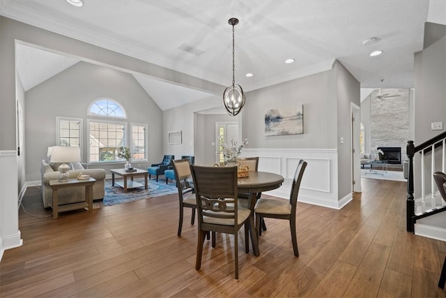 dining space featuring crown molding, a fireplace, hardwood / wood-style flooring, lofted ceiling, and ceiling fan with notable chandelier