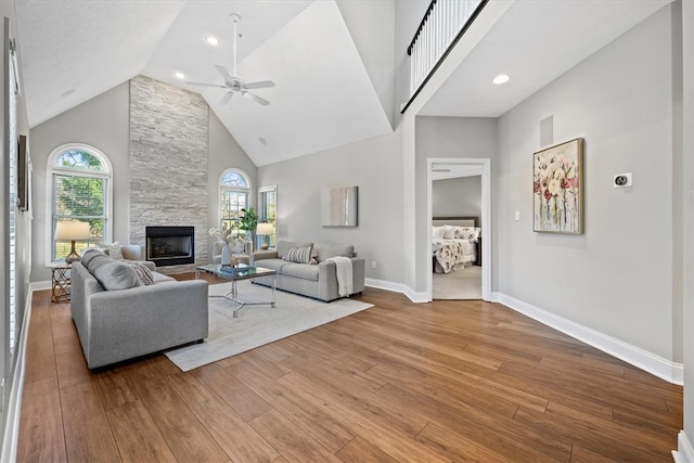 living room with high vaulted ceiling, a stone fireplace, wood-type flooring, and a healthy amount of sunlight