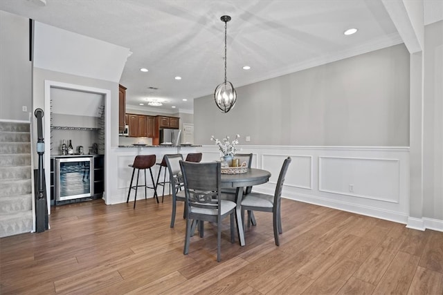 dining area featuring an inviting chandelier, wine cooler, light wood-type flooring, and ornamental molding