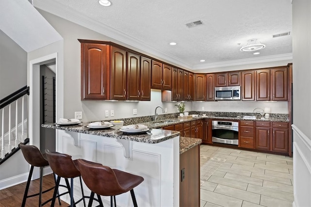 kitchen featuring dark stone counters, appliances with stainless steel finishes, a textured ceiling, sink, and kitchen peninsula