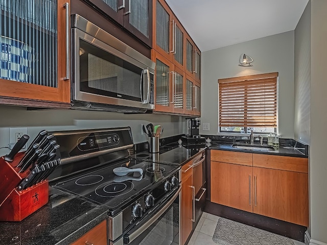 kitchen featuring appliances with stainless steel finishes, sink, dark stone countertops, and light tile patterned floors